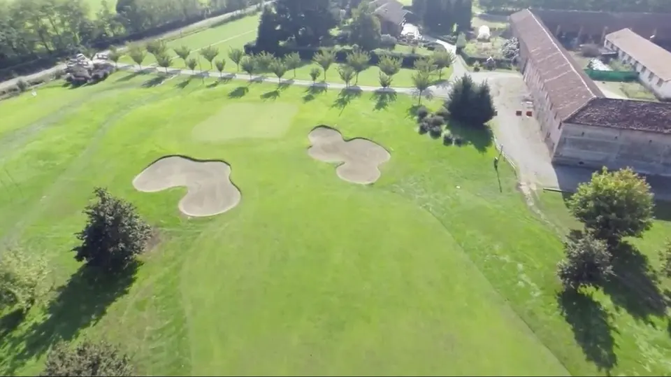 Il campo da golf con i filari e, a destra, i tetti della cascina